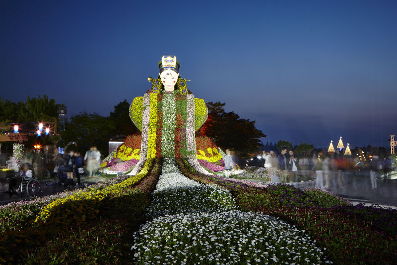 사진은 조명과 빛으로 색다른 모습을 보여주고 있는 ‘신한류 환희 정원’에 설치된 7m 높이의 새신부 조형물과 관람객들